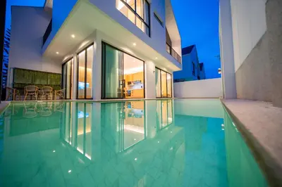 a swimming pool in front of a house at BangTao 4-Bedroom Brand New Modern Luxury Villa 2024 Minimalist Design Spacious 15-meter L-Shaped Swimming Pool Ideal for Guests in Laguna Phuket