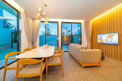 a dining room with a table and chairs and windows at BangTao 4-Bedroom Brand New Modern Luxury Villa 2024 Minimalist Design Spacious 15-meter L-Shaped Swimming Pool Ideal for Guests in Laguna Phuket