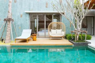 a wicker chair sitting on a deck next to a pool at Anchan Flora Luxury 2BR Pool Villa in Thalang