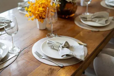 a wooden table with a white plate with a napkin and glasses at Lux Laguna Park 5 bedroom rooftop pool in Laguna Phuket