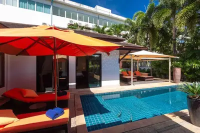 a pool with chairs and umbrellas next to a building at Sea Breeze Pool Villa on Quiet Kamala Cul de sac in Kamala Beach
