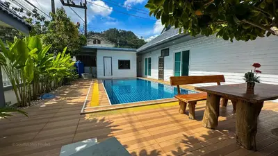 a patio with a wooden table and a swimming pool at Soulful Stay Phuket l Phanason Park Ville 1 Near Kathu Waterfall in Ban Kathu