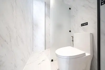 a white bathroom with a toilet and marble walls at wolin patong greeen resort in Patong Beach