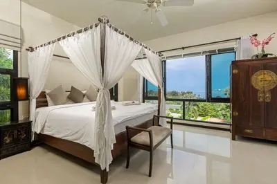 a bedroom with a canopy bed with a chair and windows at Ao Yon- Contemporary 3-bedroom private pool villa in Ban Ao Makham