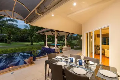 a patio with a table and chairs and a swimming pool at Peaceful 2-Bedroom Villa on Loch Palm Golf Course in Ban Kathu