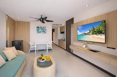 a living room with a couch and a tv on a wall at Santosa Hotel & Welness Center in Ban Kata