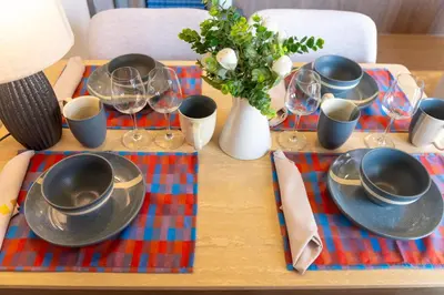a table with plates and glasses and a vase with flowers at Canvas Cherngtalay Holiday Apartments in Laguna Phuket