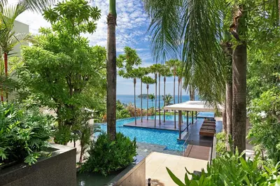 a resort swimming pool with palm trees and the ocean at The Heights C3 SeaView 2 BR, 5min to Kata Beach in Ban Karon