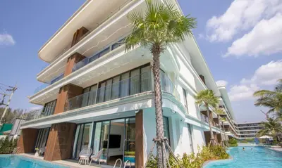 a building with a swimming pool next to a palm tree at Kora 77 2BR Beachfront Condo with Sea View and Pool in Phuket Town