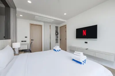 a bedroom with a white bed with a tv on the wall at Suite Anafi 2BR Pool Gym Access Ozone in Laguna Phuket