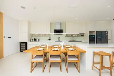 a large white kitchen with a wooden table and chairs at Taimana Luxury 3BR Private Pool Villa at LuxPride in Ban Phak Chit