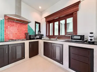 a large kitchen with brown cabinets and a microwave at ozone pool villa phuket in Ban Pa Khlok