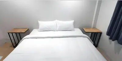 a bed with white sheets and two wooden tables at GO INN Phuket old Town in Ban Lo Long