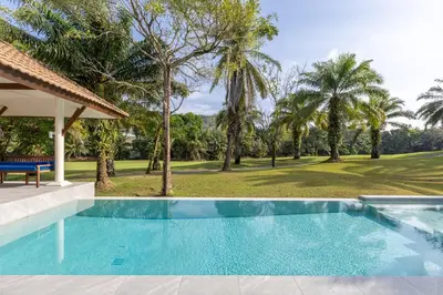 a swimming pool in front of a yard with palm trees at Elegant 2BR Pool Villa Overlooking Loch Palm Golf - Baan Sawan Garden Villa in Kathu