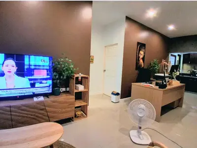 a living room with a large television and a fan at Bimi warm house in Ban Na Sat