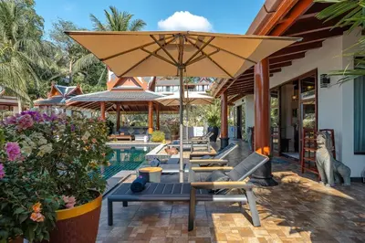 a patio with chairs and an umbrella next to a pool at Arun Rapee Villa Surin Beach in Surin Beach