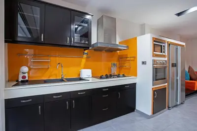 a kitchen with black cabinets and an orange wall at 3 BR Pool Villa Kloua near Chalong Temple in Ban Na Bon