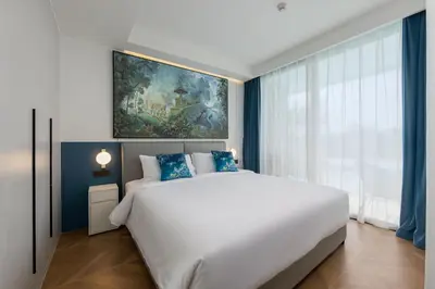 a bedroom with a large white bed with blue accents at Tinos 1BR Suite at Kora Beach Resort in Layan Beach
