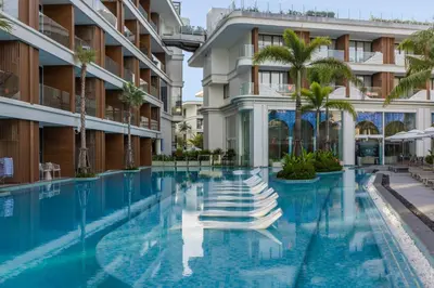 a swimming pool with chaise lounges in front of a building at Tinos 1BR Suite at Kora Beach Resort in Layan Beach
