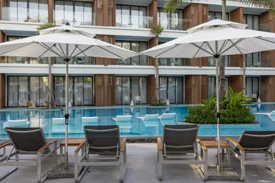 a pool with chairs and umbrellas in front of a building at Tinos 1BR Suite at Kora Beach Resort in Layan Beach