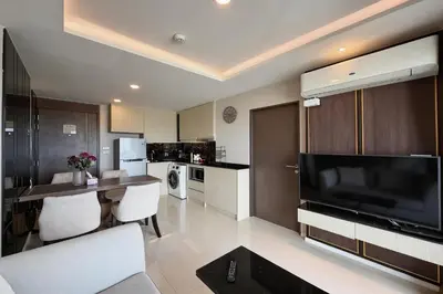 a living room with a large television and a kitchen at Mida Grande Surin Private Suites in Ban Lum Fuang