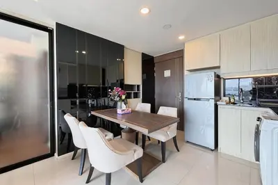 a kitchen with a wooden table and white chairs at Mida Grande Surin Private Suites in Ban Lum Fuang