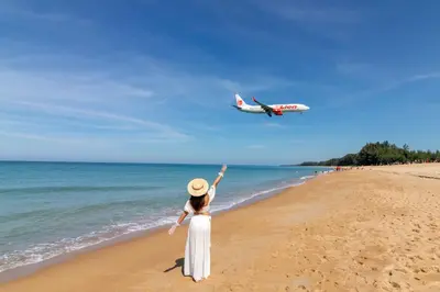 a woman on a beach with an airplane flying over the ocean at Proud Phuket, Naiyang Beach in Nai Yang Beach