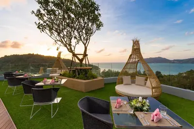 a group of tables and chairs on a balcony with the ocean at Crest Resort & Pool Villas - SHA Extra Plus in Patong Beach