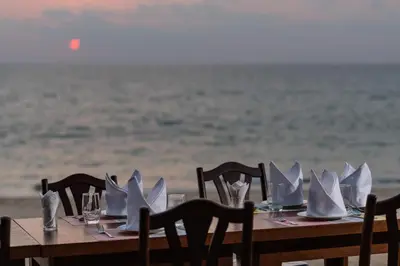 a table with white plates and napkins on the beach at Coriacea Beachfront Boutique Phuket Resort in Mai Khao Beach