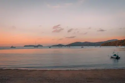 a boat in the water at sunset on the beach at The Cove in Panwa Beach