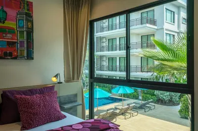 a bedroom with a large window with a view of a building at Apartments in The Title Beach Rawai in Rawai Beach