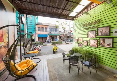 a green building with tables and chairs and a motorcycle at 217@HKT in Phuket Town