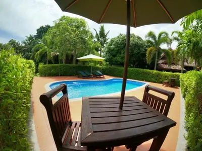 a wooden table with an umbrella next to a pool at Cozy Garden Resort in Ao Nang Beach
