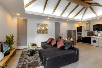 a living room with a black couch and a kitchen at La Ville Phuket Pool Villa in Nai Yang Beach