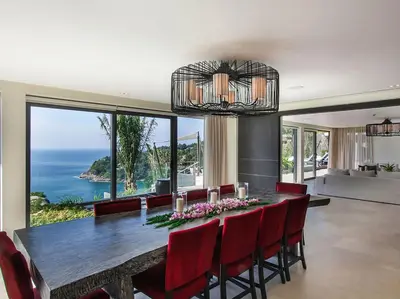 a dining room with a table and chairs and a large window at Villa Saan - SHA Extra Plus in Kamala Beach