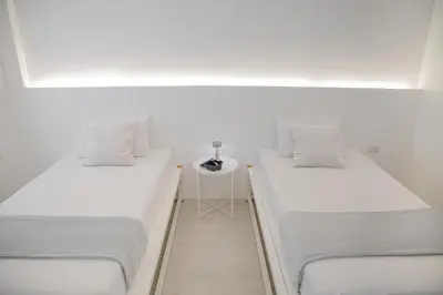 two beds in a white room with a table at Hao Hostel Phuket in Phuket Town