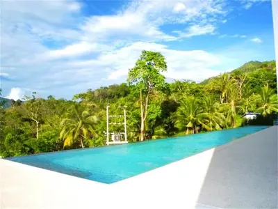 a swimming pool with blue water in front of trees at Patong Bay Hill 1 bedroom Apartment in Patong Beach