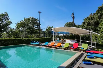 a swimming pool with colorful chairs and an umbrella at Naiharn Beach Resort - SHA Plus Extra in Nai Harn Beach