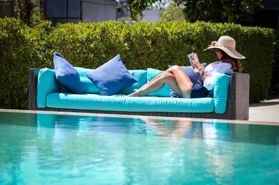 a woman sitting on a couch next to a swimming pool at Naiharn Beach Resort - SHA Plus Extra in Nai Harn Beach