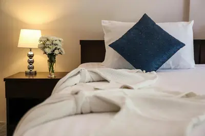 a white bed with a blue pillow and a vase of flowers at Naiharn Beach Resort - SHA Plus Extra in Nai Harn Beach