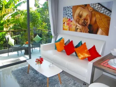 a living room with a white couch with colorful pillows at Emerald Patong 1 bedroom Apartment Garden View in Patong Beach
