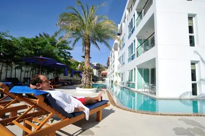 a man laying on a chair next to a swimming pool at The Palms, Kamala Beach - SHA Extra Plus in Kamala Beach
