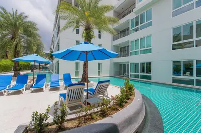 a swimming pool with chairs and umbrellas next to a building at The Palms, Kamala Beach - SHA Extra Plus in Kamala Beach