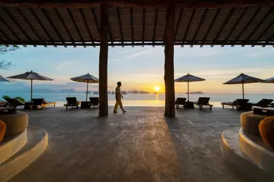 a man walking on the beach with the sunset in the background at Six Senses Yao Noi in Ko Yao Noi