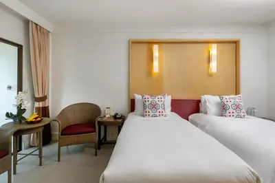 a hotel room with two beds and a chair at Sawaddi Patong Resort & Spa by Tolani in Patong Beach