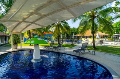 a pool with a green umbrella and chairs and palm trees at Sunwing Kamala Beach in Kamala Beach