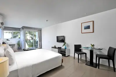 a white bedroom with a bed and a desk and chairs at Nap Patong in Patong Beach