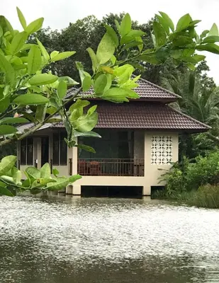a house on the water with trees in the foreground at Lantala Residence in Natai Beach