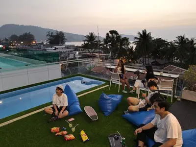 a group of people sitting on the grass by a swimming pool at BearPacker Patong Hostel in Patong Beach