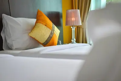 a bed with an orange pillow and a lamp on it at Naiyang Place - Phuket Airport in Nai Yang Beach